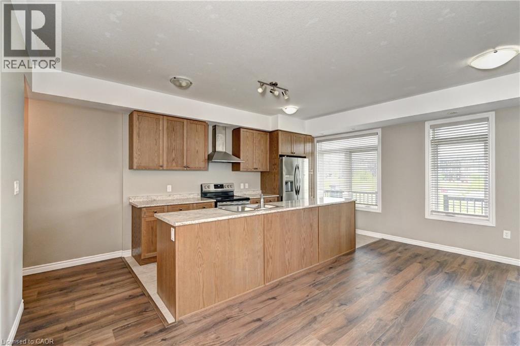 Open-concept kitchen and dining area featuring warm wood-finish cabinetry, stainless steel appliances, quartz countertops, a substantial center island with seating, and wood-finish flooring throughout - 102 Wheat Lane, Kitchener, ON
