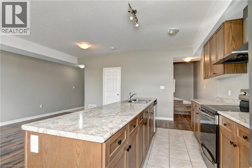 Spacious kitchen featuring a large center island with wood cabinetry and a white quartz countertop, stainless steel appliances, recessed and track lighting, and hard-surface flooring throughout the op - 102 Wheat Lane, Kitchener, ON
