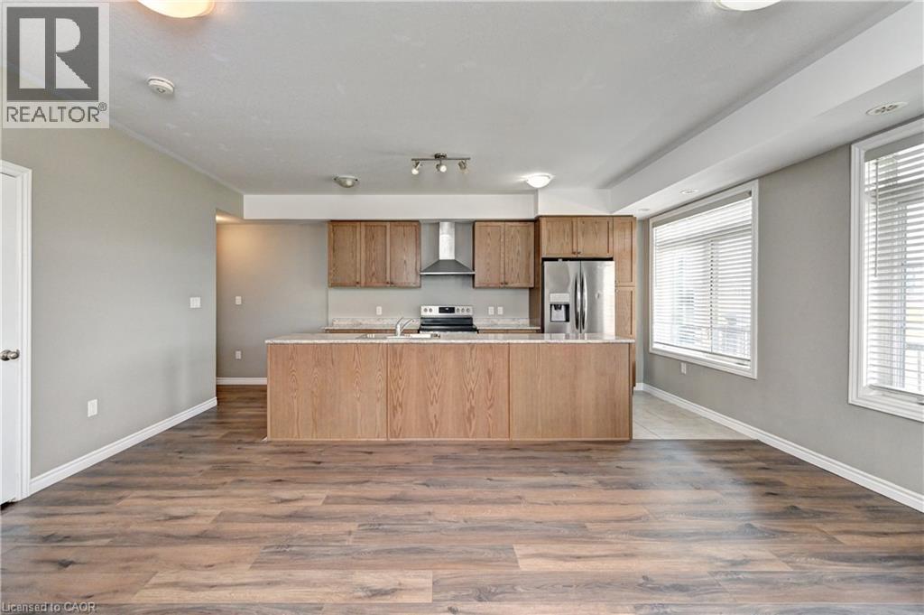 Open-concept kitchen and dining area featuring wood-finish cabinetry, stainless steel appliances, a center island with seating, and wood-finish plank flooring throughout - 102 Wheat Lane, Kitchener, ON
