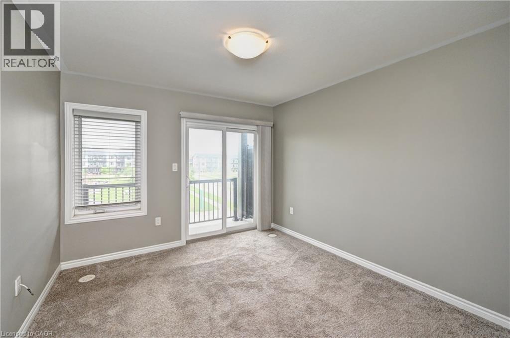 Plush carpet flooring, neutral wall tones, crown molding, and a sliding glass door leading to a balcony - 102 Wheat Lane, Kitchener, ON