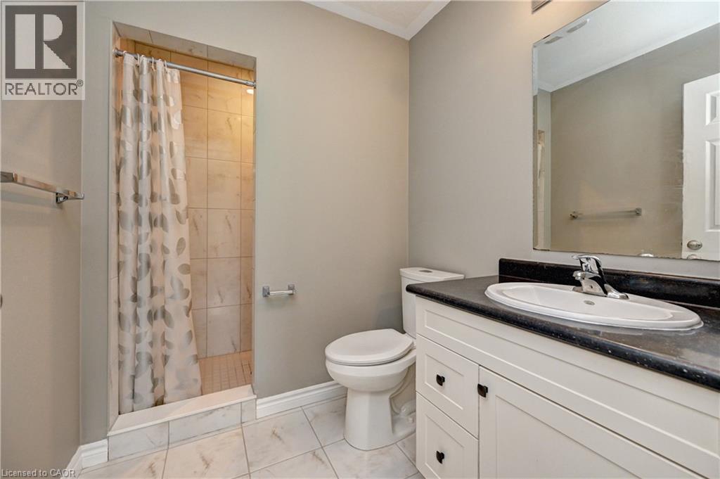 Tiled shower enclosure, white vanity with black countertop, integrated sink, large wall mirror, and white tile flooring - 102 Wheat Lane, Kitchener, ON
