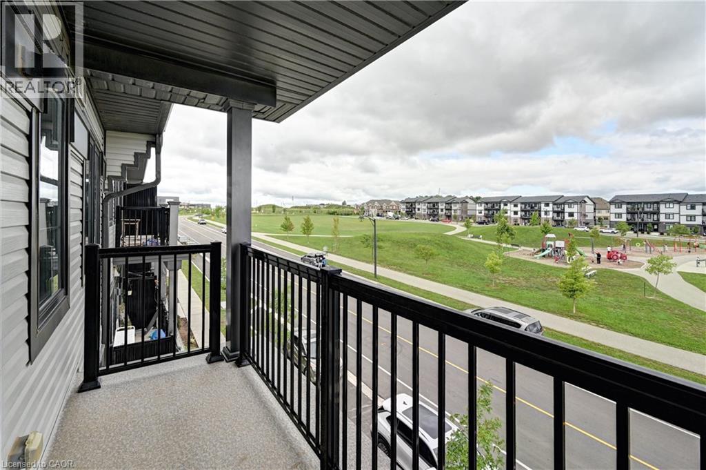 Spacious covered balcony with black aluminum railing overlooking expansive green space and new residential development - 102 Wheat Lane, Kitchener, ON