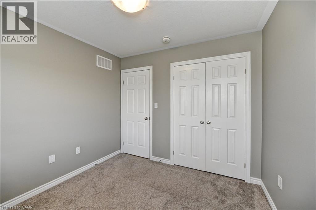 Neutral-toned walls with carpet flooring, featuring a paneled door and bi-fold closet doors - 102 Wheat Lane, Kitchener, ON