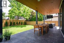 Covered outdoor patio featuring stone tile flooring, a wood-finish ceiling with recessed lighting, and support columns - 