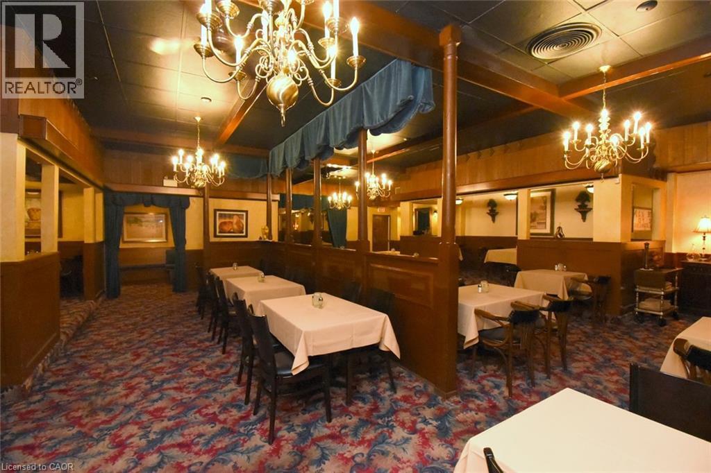 Elegant dining space featuring wood-paneled walls, ornate crystal chandeliers, and a patterned area rug - 942-946 Barton Street E, Hamilton, ON