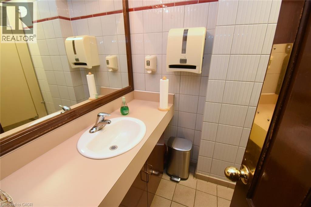 Bathroom featuring a round pedestal sink with chrome faucet, expansive countertop space, large framed mirror, white subway tile walls with contrasting trim detail, and multiple wall-mounted dispensers - 942-946 Barton Street E, Hamilton, ON