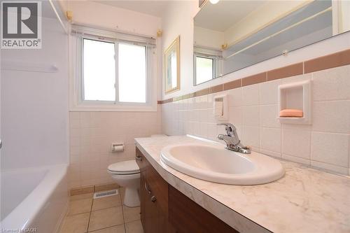 Bathroom featuring a bathtub, toilet, vanity with integrated sink, large mirror, and a window - 98 Kennedy Avenue, Hamilton, ON 