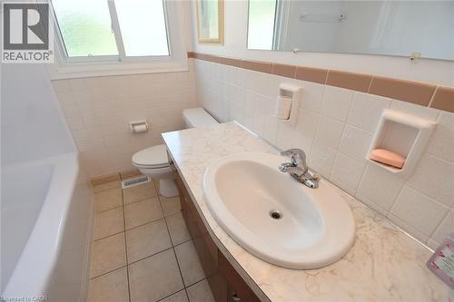 Bathroom featuring a built-in vanity with integrated sink, chrome faucet, tiled flooring, and a window - 98 Kennedy Avenue, Hamilton, ON 