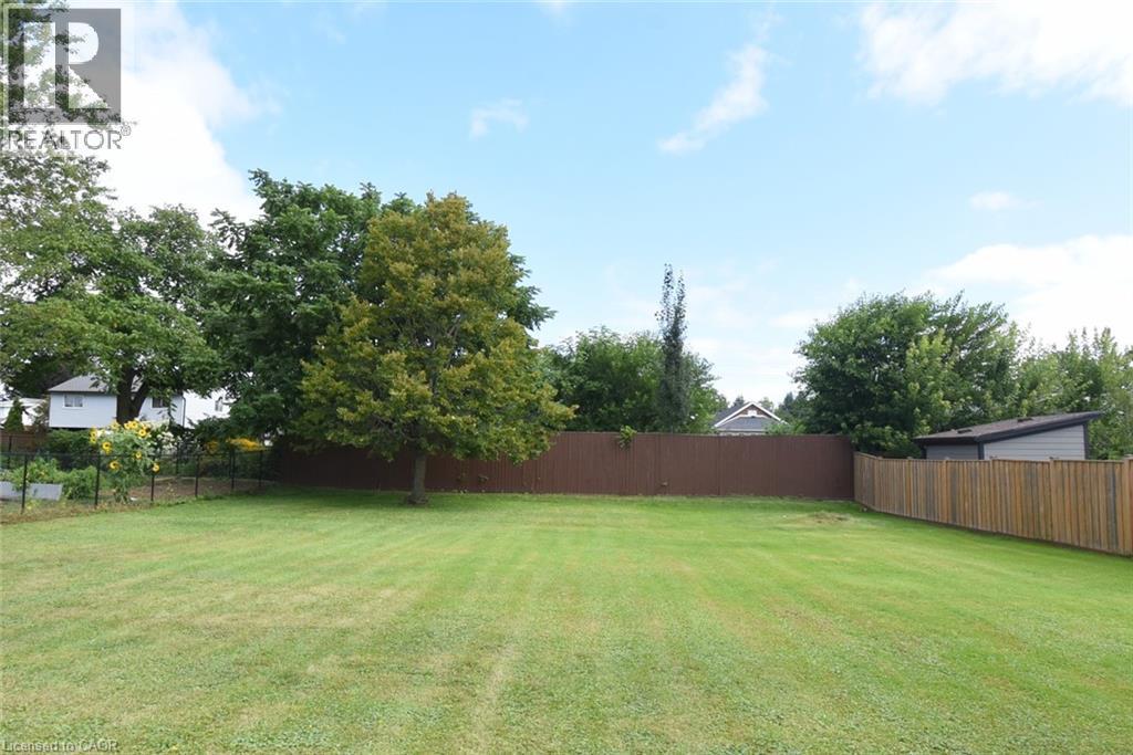 Expansive grounds featuring a level, manicured lawn bordered by mature trees and sturdy wood-finish fencing - 98 Kennedy Avenue, Hamilton, ON