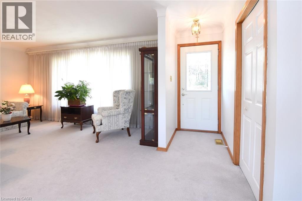 Spacious living area with wall-to-wall carpeting, abundant natural light from large windows dressed in sheer curtains, wood-trimmed doorways, and recessed ceiling lighting - 98 Kennedy Avenue, Hamilton, ON