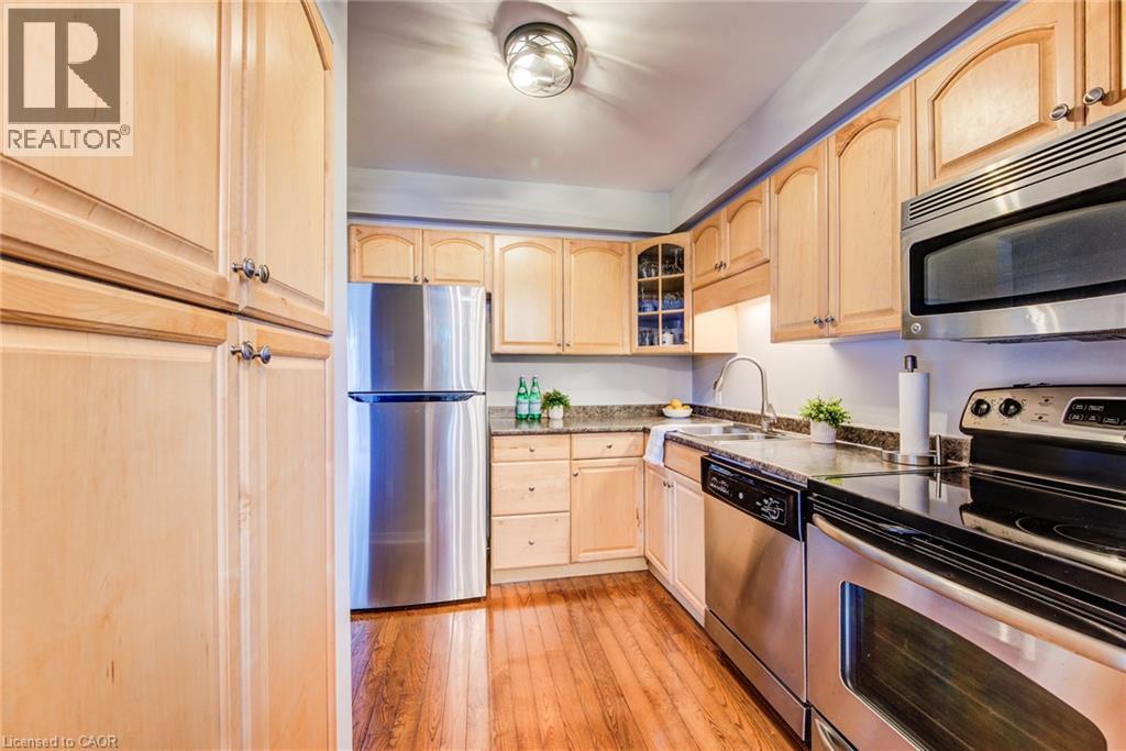 Kitchen featuring wood-finish flooring, light wood cabinetry, stainless steel appliances, and dark stone countertops - 360 Cornridge Place Unit# 2, Waterloo, ON