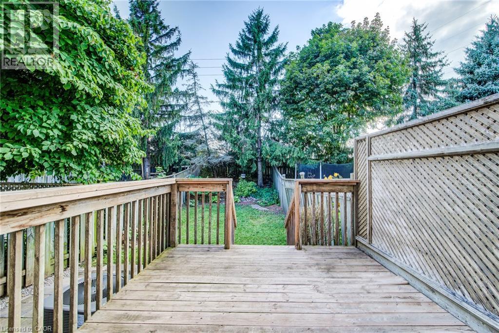 Wood deck with railings and steps providing access to a grassy yard, bordered by mature trees and a lattice privacy screen - 360 Cornridge Place Unit# 2, Waterloo, ON