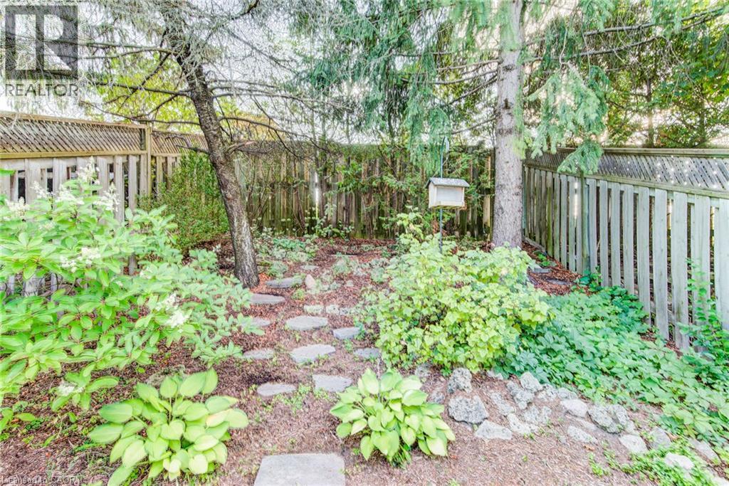 Fenced yard with mature trees, established plantings, and stone pavers - 360 Cornridge Place Unit# 2, Waterloo, ON