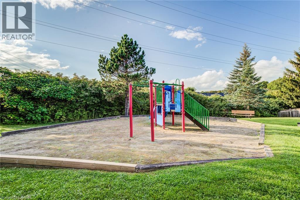Recreational play structure with slide and climbing features, set within a sand-filled area, surrounded by a manicured lawn - 360 Cornridge Place Unit# 2, Waterloo, ON