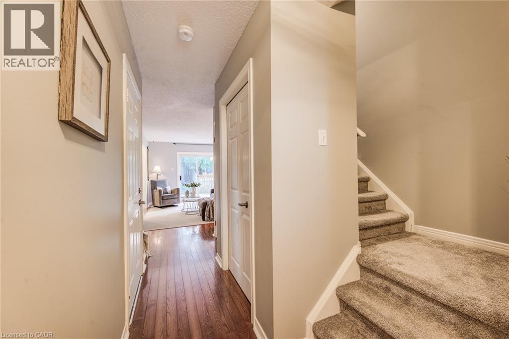 Hallway with wood-finish flooring, white doors, and a carpeted staircase - 360 Cornridge Place Unit# 2, Waterloo, ON