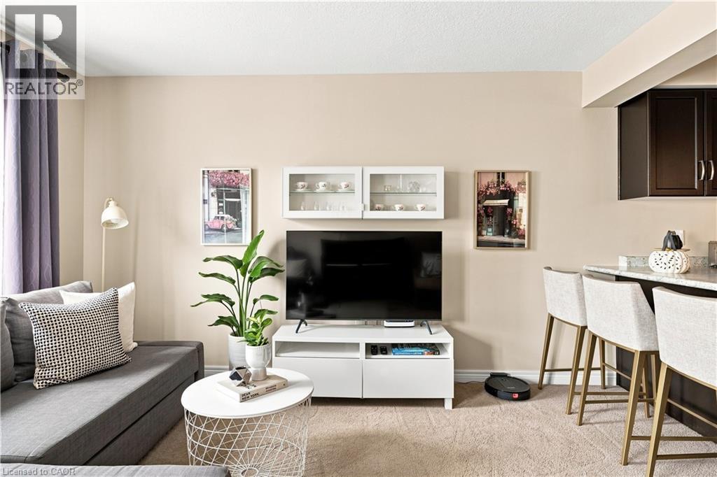 Modern open-concept living space featuring a wall-mounted flat-screen television, built-in white cabinetry with integrated storage, pendant lighting, neutral wood-finish flooring, and a dedicated kitc - 187 Eden Oak Trail, Kitchener, ON