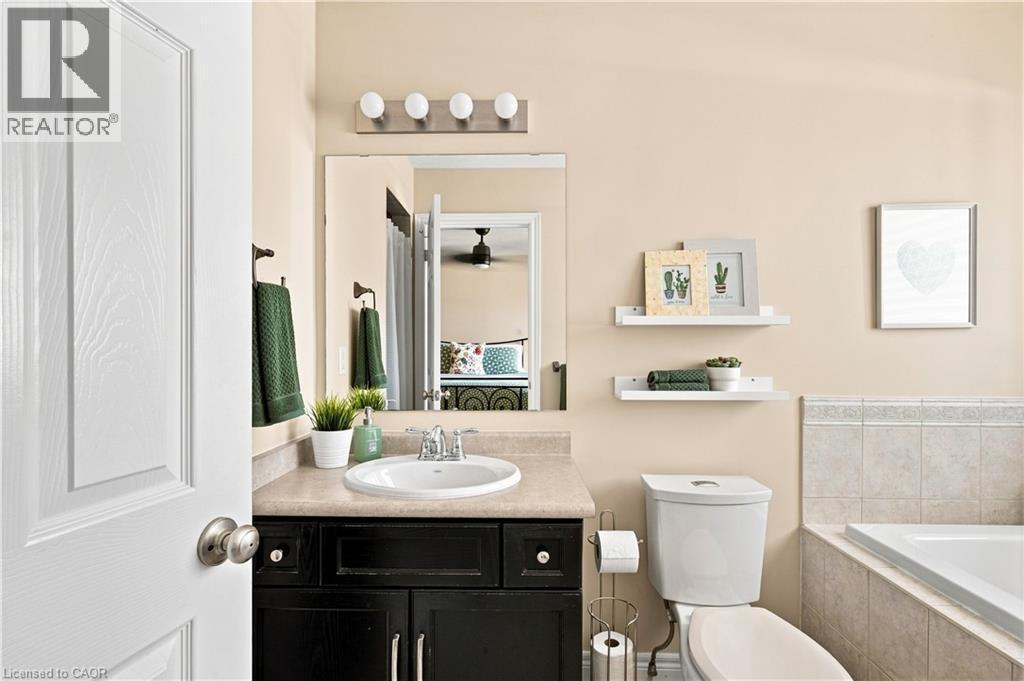 Bathroom featuring a dark wood-finish vanity with an integrated sink and light-toned countertop, a wall-mounted mirror, and a built-in bathtub with tiled surround - 187 Eden Oak Trail, Kitchener, ON