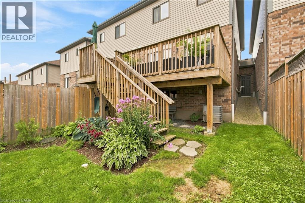 Expansive wood deck with stairs, brick and siding exterior, established garden beds, grassy lawn, and wood fencing - 187 Eden Oak Trail, Kitchener, ON