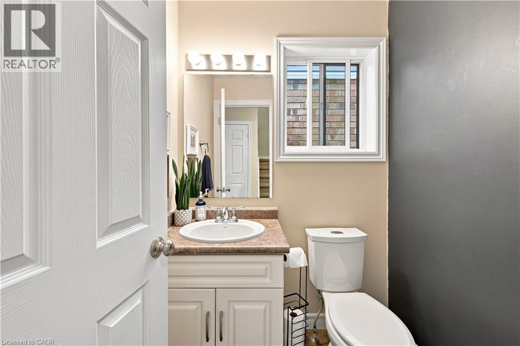 White single-panel door, integrated vanity with single sink and countertop, wall-mounted mirror with overhead lighting, and a white toilet - 187 Eden Oak Trail, Kitchener, ON