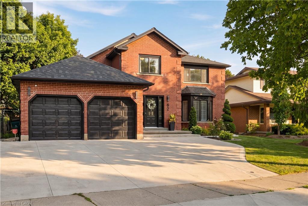 Red brick exterior with a two-car garage, black garage doors, bay window, concrete driveway, and front landscaping - 62 Corfield Drive, Kitchener, ON