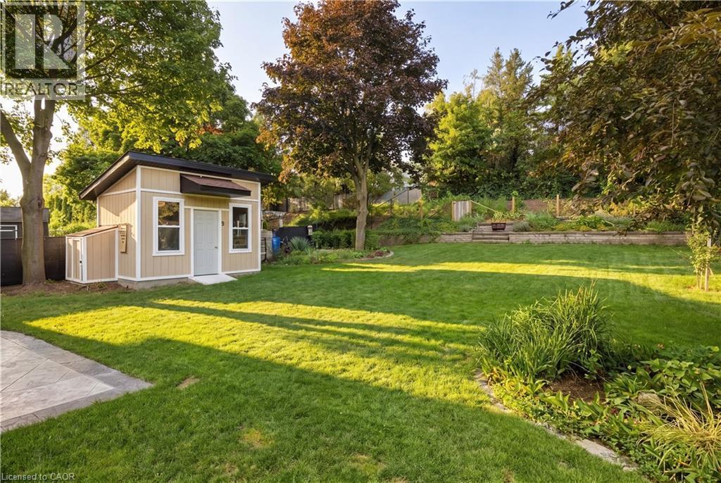 Expansive backyard featuring a manicured lawn, a detached shed with a shallow-pitched roof, and a tiered garden area with natural stone steps - 62 Corfield Drive, Kitchener, ON