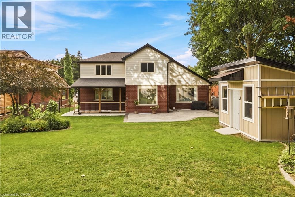 Expansive lawn area, brick and siding exterior, covered porch with railing, concrete patio, and detached storage shed - 62 Corfield Drive, Kitchener, ON