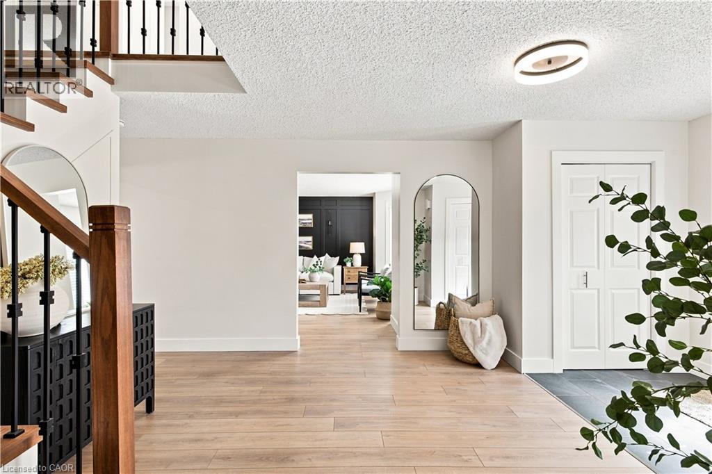 Wood-finish flooring, staircase with dark wood newel post and wrought iron spindles, contemporary ceiling light fixture, and white paneled doors - 62 Corfield Drive, Kitchener, ON