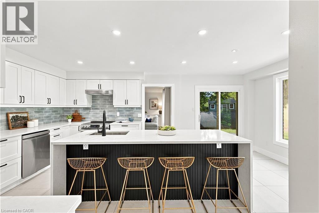 Modern kitchen featuring white shaker cabinetry, stainless steel appliances, a light blue tile backsplash, and a large island with a white countertop - 62 Corfield Drive, Kitchener, ON