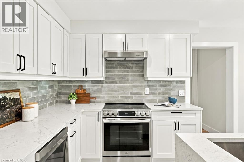 White shaker-style cabinetry with matte black hardware, light-toned countertops, full-height gray subway tile backsplash, and stainless steel appliances - 62 Corfield Drive, Kitchener, ON