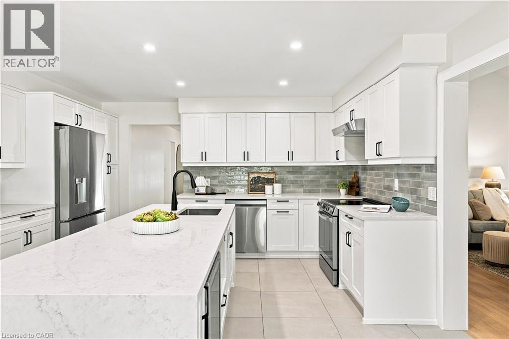 Kitchen featuring white shaker cabinetry, stainless steel appliances, a large center island with a black faucet, and a subway tile backsplash - 62 Corfield Drive, Kitchener, ON