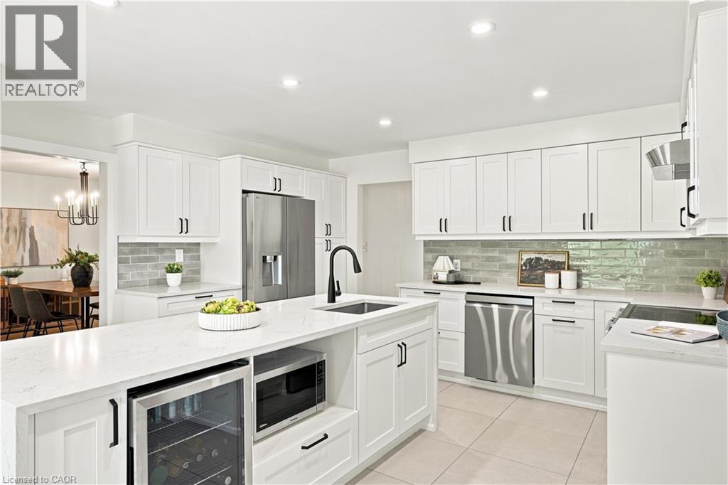 White shaker cabinetry, light-toned tile flooring, center island with integrated beverage cooler, stainless steel appliances, and a tiled backsplash - 62 Corfield Drive, Kitchener, ON