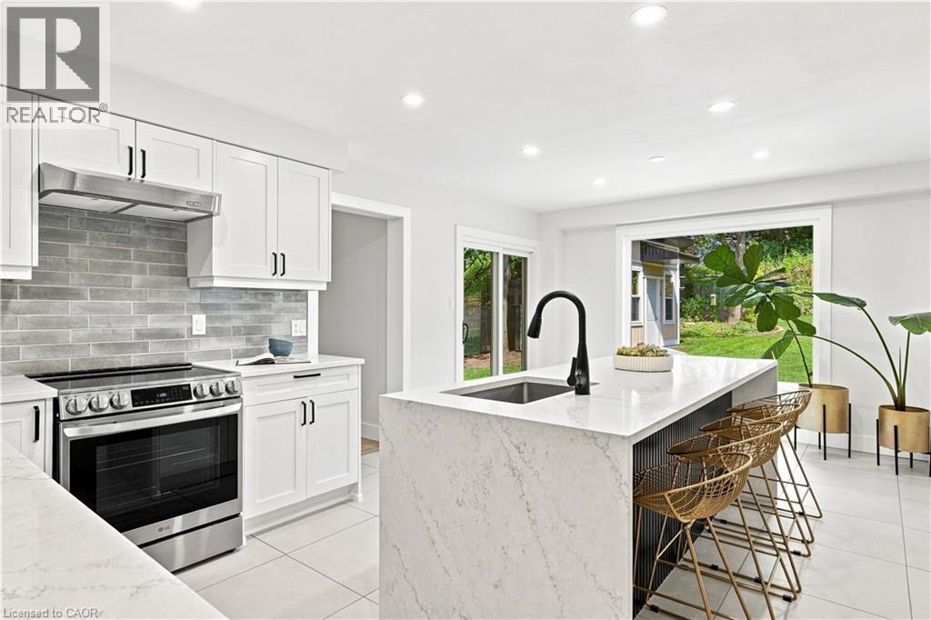 Modern kitchen featuring white shaker-style cabinetry, a stainless steel range with a coordinating vent hood, and a gray subway tile backsplash - 62 Corfield Drive, Kitchener, ON