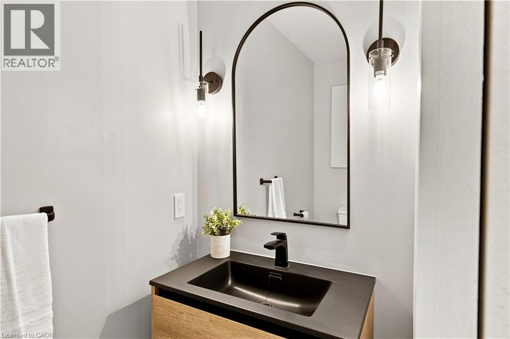 Arched mirror with black frame, wood-finish vanity, matte black faucet, dark basin, and wall-mounted light fixtures - 62 Corfield Drive, Kitchener, ON