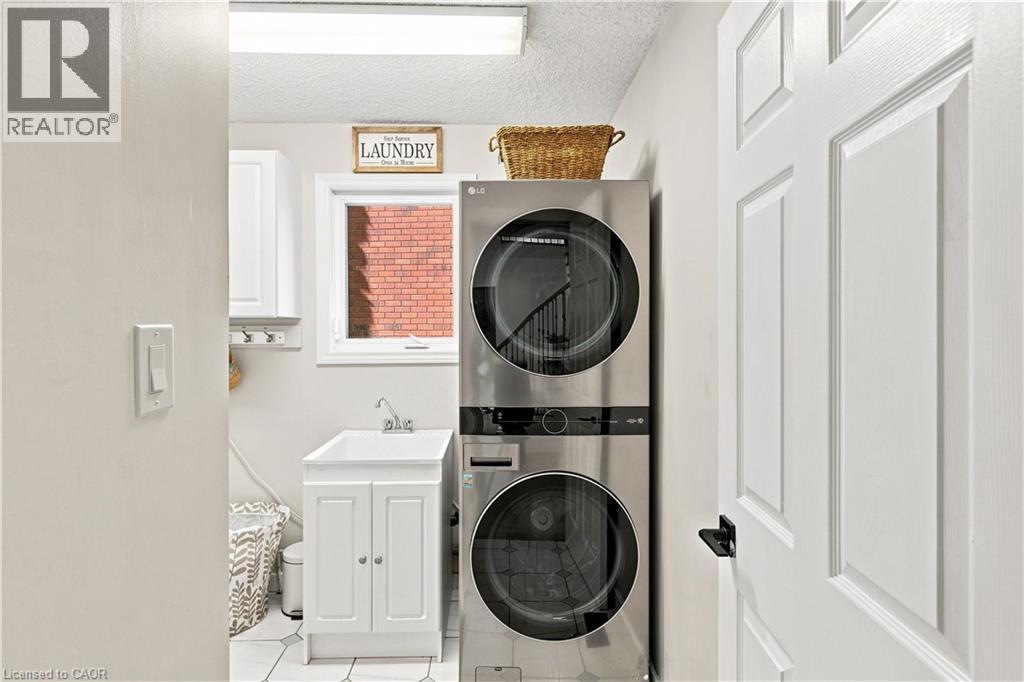 Stainless steel stackable washer and dryer, white utility sink, white base cabinetry with brushed nickel hardware, and white wall cabinetry - 62 Corfield Drive, Kitchener, ON
