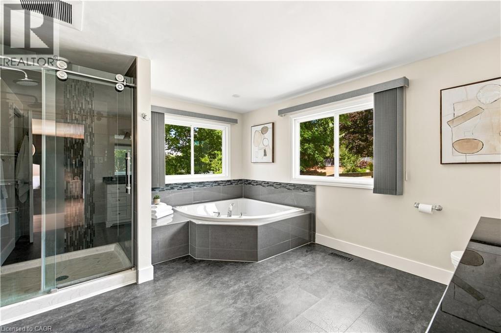 Spacious bathroom featuring a corner soaking tub, large glass-enclosed shower, dual windows, and dark tile flooring - 62 Corfield Drive, Kitchener, ON