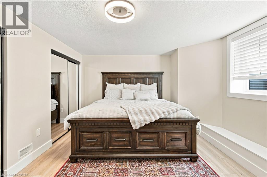 Recessed window with white blinds, light-toned wood-finish flooring, sliding mirrored closet doors, and a contemporary ceiling fixture - 62 Corfield Drive, Kitchener, ON