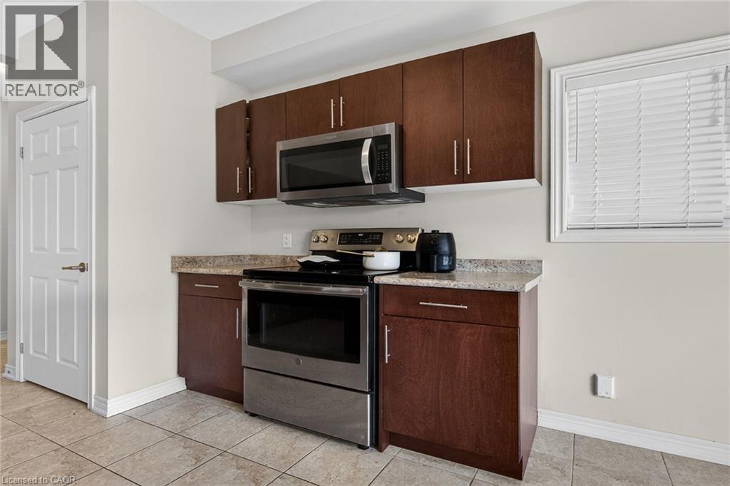 Stainless steel range and microwave, wood-finish cabinetry, light-toned countertop, and tiled flooring - 9 Winterberry Boulevard, Thorold, ON
