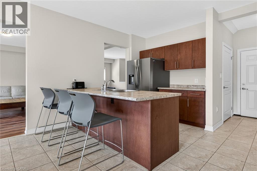 Kitchen featuring wood-finish cabinetry, stainless steel refrigerator, and a breakfast bar with stone-finish countertop - 9 Winterberry Boulevard, Thorold, ON