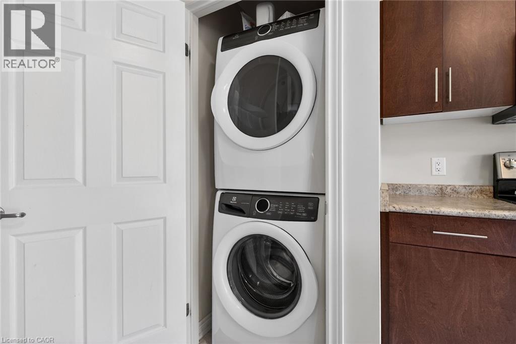 Full-size stacked washer and dryer in a dedicated closet, alongside wood-finish cabinetry and a stone-finish countertop - 9 Winterberry Boulevard, Thorold, ON