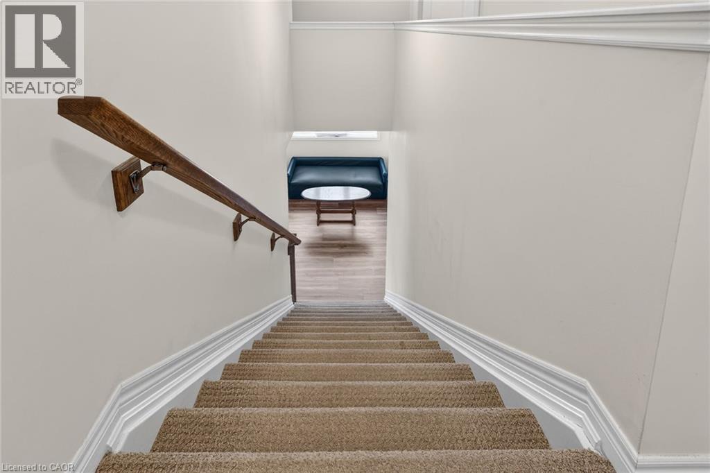 Carpeted stairs with a wood handrail, white trim, and light wall finishes - 9 Winterberry Boulevard, Thorold, ON