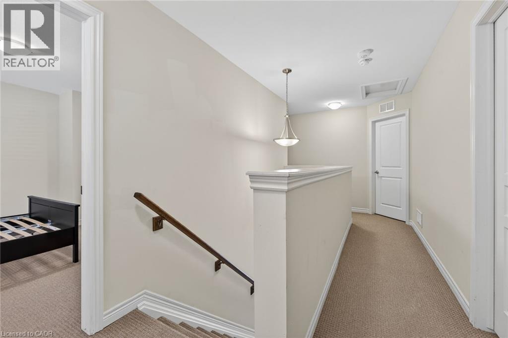 Carpeted hallway featuring a pendant light fixture, white trim, and a wood handrail - 9 Winterberry Boulevard, Thorold, ON