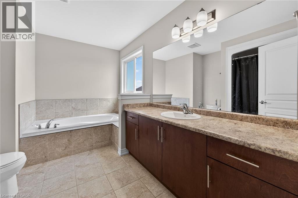 Built-in bathtub with tiled surround, large vanity with integrated sink, expansive mirror, and overhead lighting - 9 Winterberry Boulevard, Thorold, ON