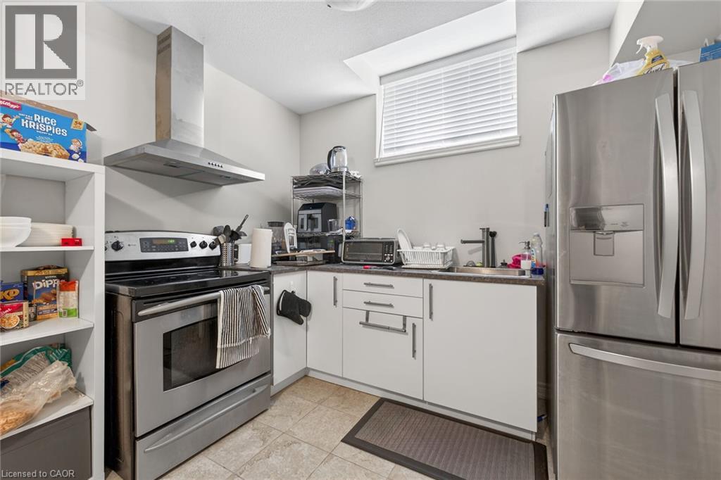 Stainless steel range with coordinating range hood, stainless steel refrigerator, white cabinetry, dark countertops, and tile flooring - 9 Winterberry Boulevard, Thorold, ON