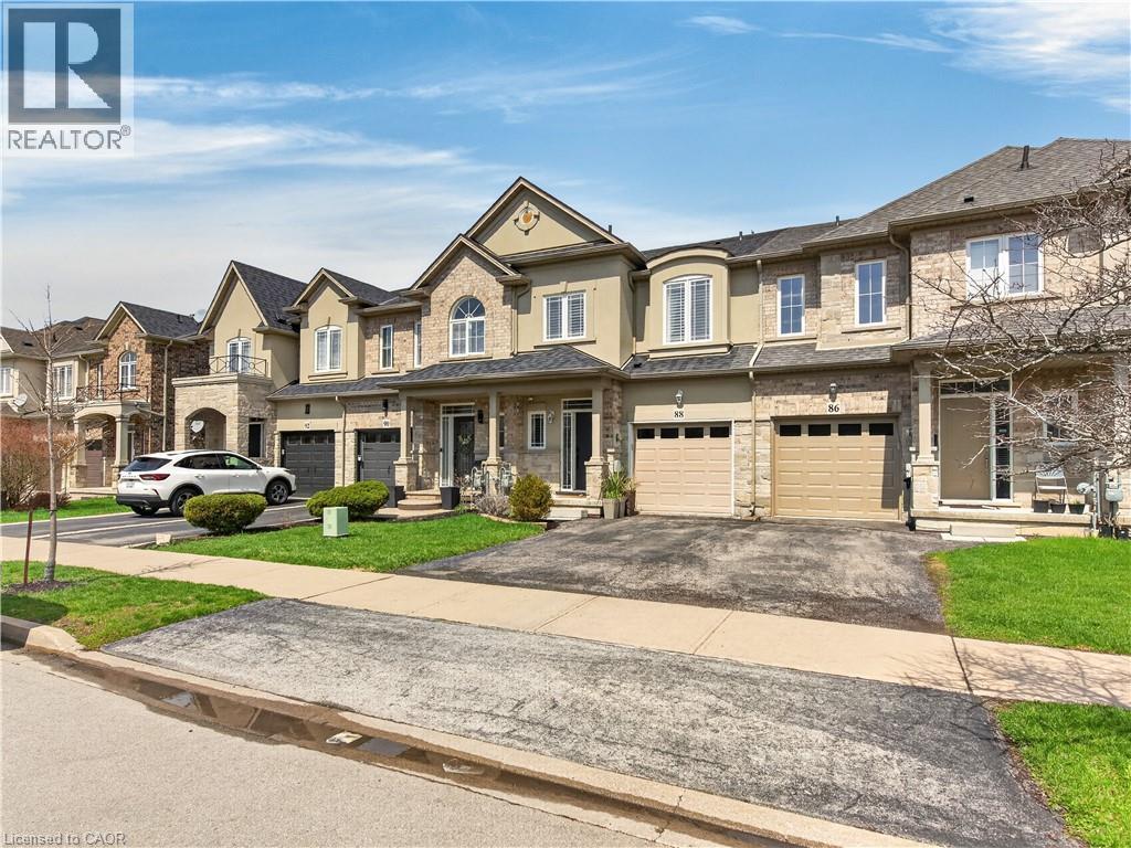 Exterior featuring a combination of brick and stucco finishes, multiple gabled rooflines, attached garages, and a front porch entry - 88 Highgate Drive, Hamilton, ON