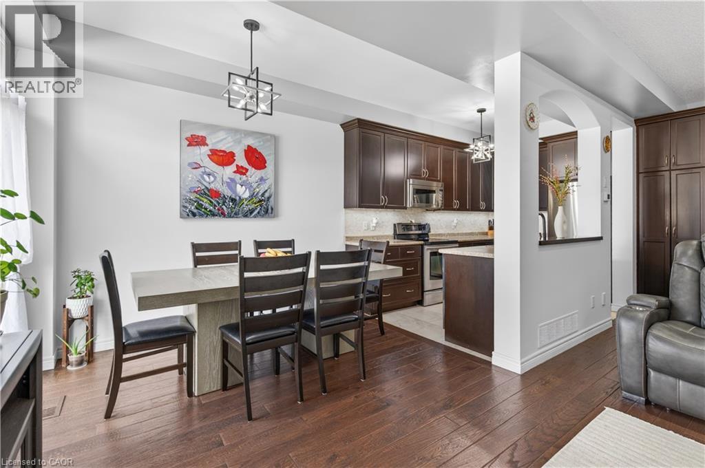Wood-finish flooring throughout, dining area with a contemporary chandelier, open-concept kitchen with stainless steel appliances, dark wood cabinetry, and a light-toned backsplash - 88 Highgate Drive, Hamilton, ON