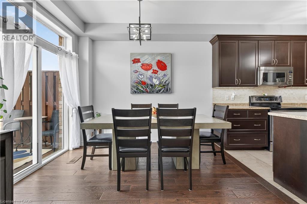 Open-concept space featuring wood-finish flooring, a sliding glass door for outdoor access, dark wood cabinetry, and a built-in stainless steel microwave - 88 Highgate Drive, Hamilton, ON