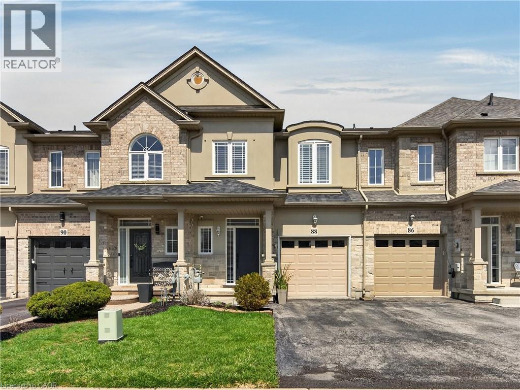 Two-story townhome featuring a stone and stucco exterior, arched windows, covered front entrance, and an attached single-car garage - 88 Highgate Drive, Hamilton, ON