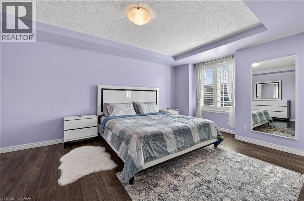 Tray ceiling, recessed lighting, wood-finish flooring, window with white plantation shutters, and a modern white headboard - 88 Highgate Drive, Hamilton, ON