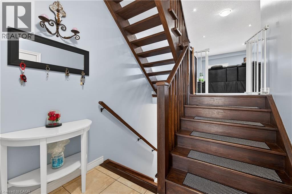 Hardwood staircase with natural wood balusters, tile flooring, and a wall-mounted handrail - 88 Highgate Drive, Hamilton, ON