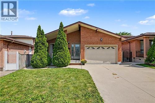 Brick exterior with an attached garage, paved driveway, and mature landscaping - 14 Indian Crescent, Hamilton, ON 
